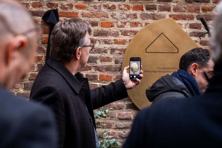 Inhuldiging gedenkpaneel restauratiecampagne waarbij een man een foto trekt van het paneel