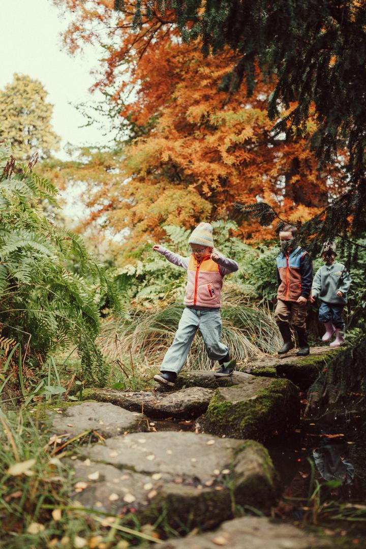 Kinderen stappen over de stapstenen van het Arboretum in de herfst