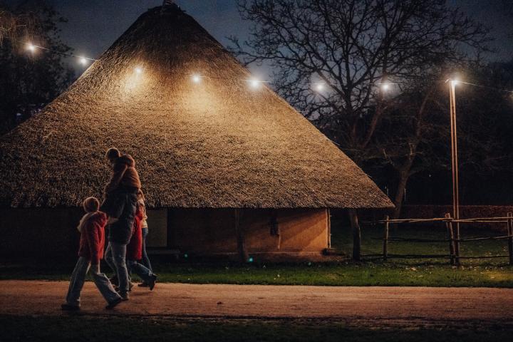 Gezin wandelt voor verlicht historisch gebouw door waar ook een gezellige lichtslinger naast het pad hangt