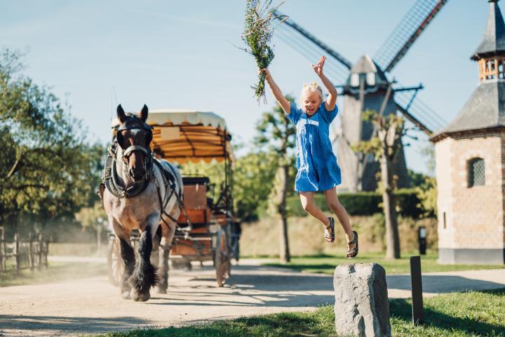 Meisje springt met boeket bloemen terwijl huifkar met boerenpaard langs rijdt