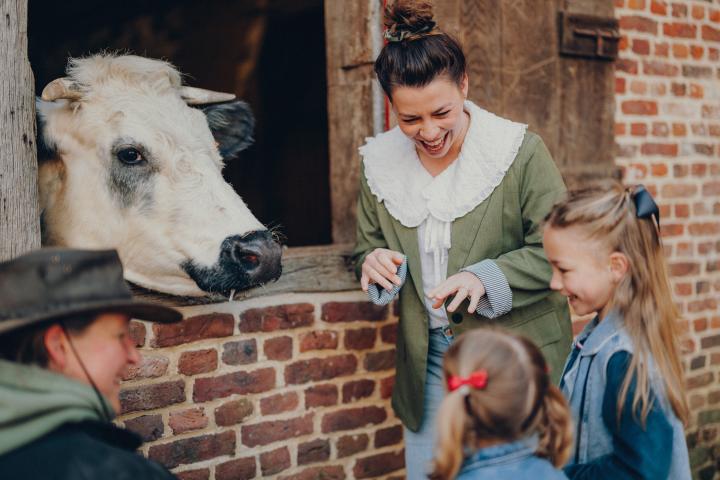 Mama en dochters kijken naar een koe die haar hoofd uit de stal steekt