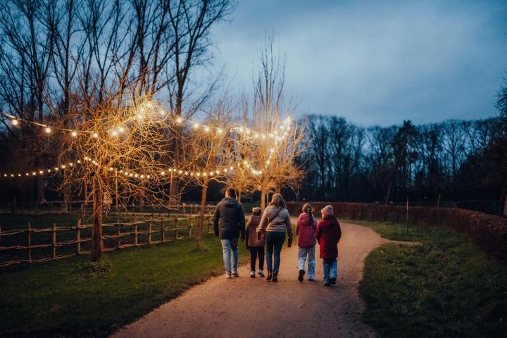 Gezin wandelt over pad kijkend naar de lichtslingers in de bomen naast het pad 