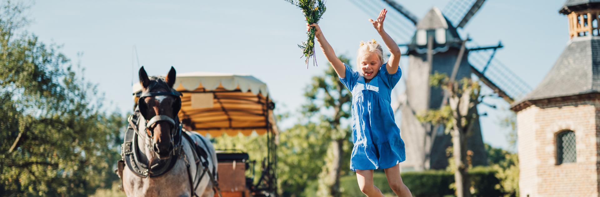 Kind springt van paaltje terwijl de huifkar met boerenpaard voorbij rijdt