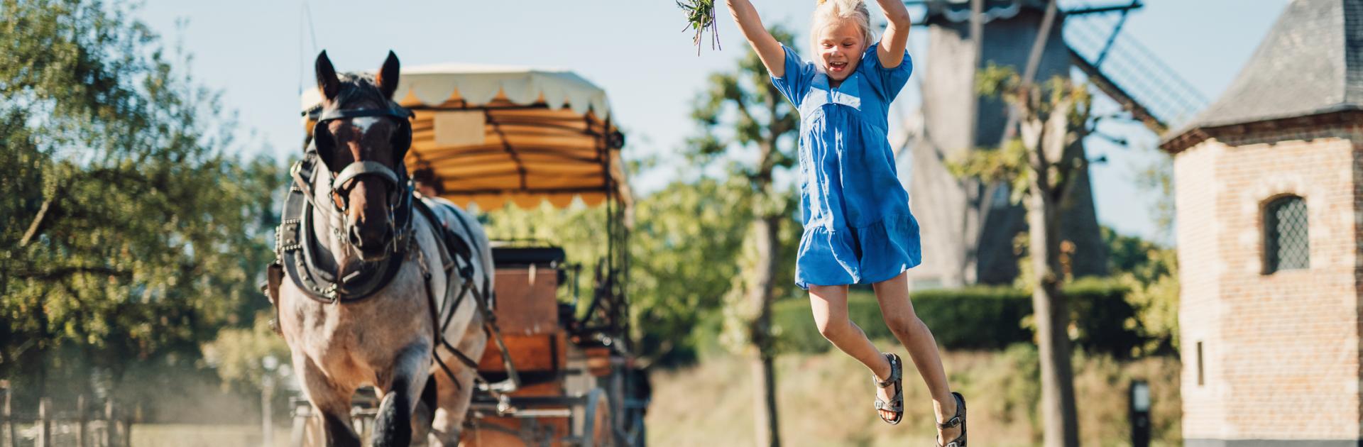 Kind springt van paaltje terwijl de huifkar met boerenpaard voorbij rijdt