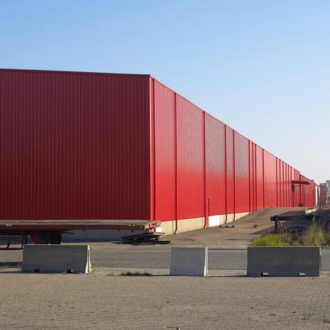 Zijaanzicht renovatie daken en wanden van magazijn TCL. De wanden van het magazijn zijn rood. Tijdens de renovatie werd er staal gebruikt.