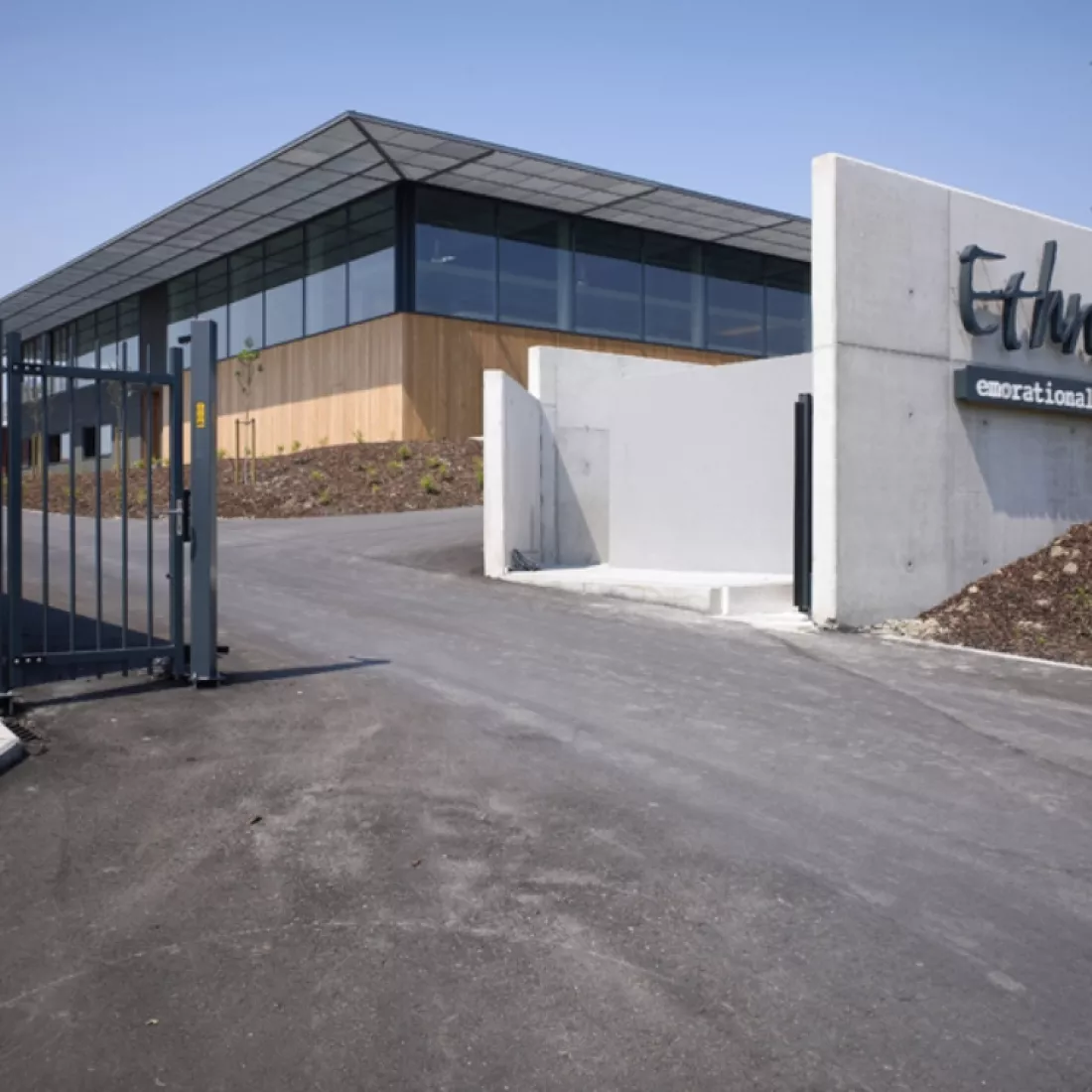 Poort magazijnruimte met kantoor - Ethnicraft. Rond het gebouw staat een zwarte poort en een betonnen muur. Tegen de muur hangt het logo van Ethnicraft.