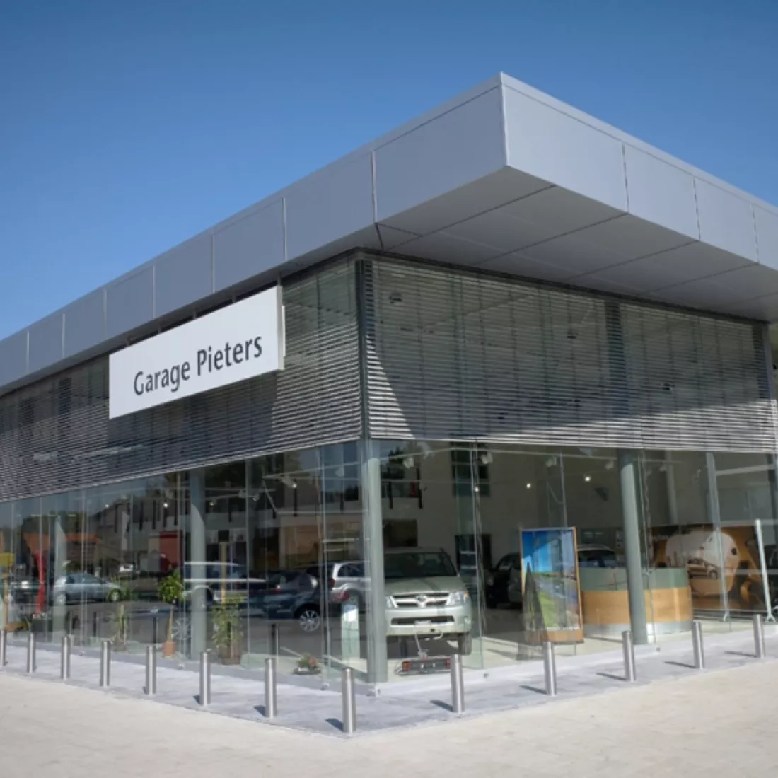Zijaanzicht showroom garage Pieters. De showroom bestaat uit grote ramen. Tegen het gebouw hangt een wit bord. Op het bord staat 'garage Pieters' in zwarte letters.