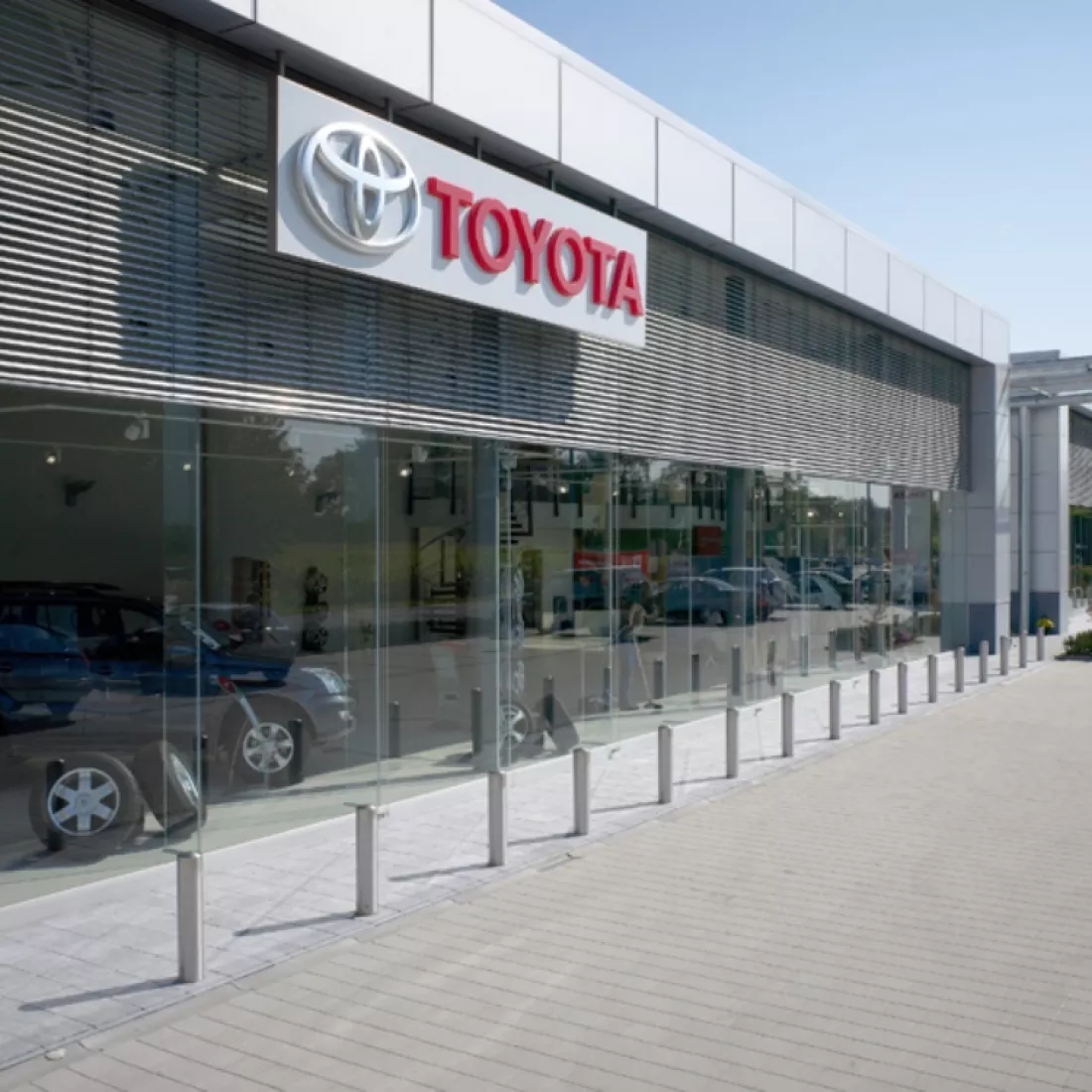 Zijaanzicht showroom garage Pieters. De showroom bestaat uit grote ramen. Tegen het gebouw hangt het logo van Toyota.