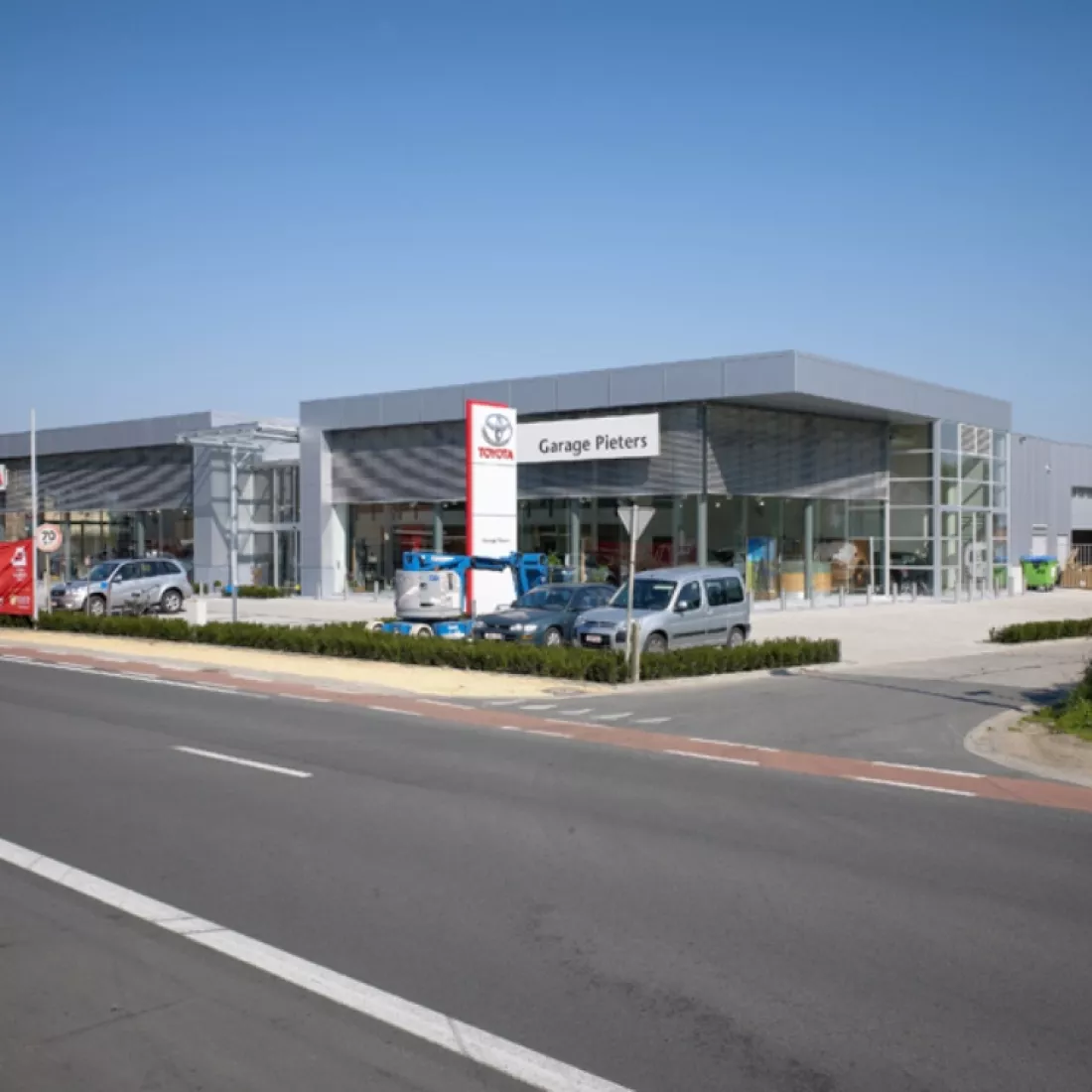 Showroom, carrosserie en kantoor garage Pieters. Het gebouw is grijs en bestaat bijna volledig uit ramen bij de showroom. Voor het gebouw is parkeerruimte voorzien. Er staat ook een wit met rood bord voor het gebouw. Hierop staat het logo van Toyota. Aan het gebouw zelf hangt een wit bord met garage Pieters erop.