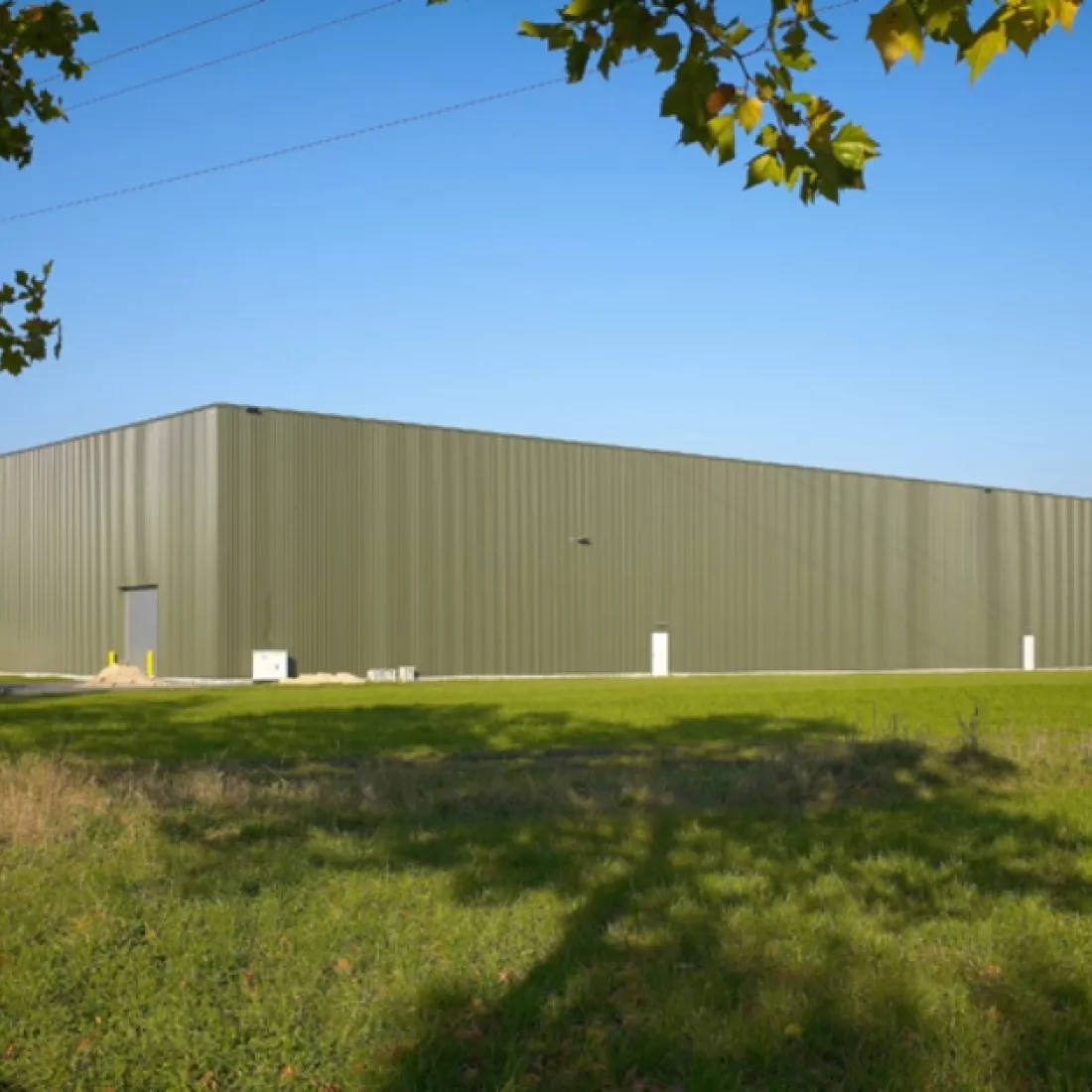 Zijaanzicht opslagloodsen - Mintjens. De loodsen bestaan uit groene platen. Rond de loodsen bevindt zich gras.
