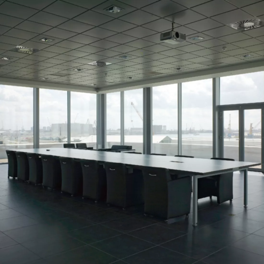 Vergaderruimte in kantoorgebouw Nova Natie HQ. De buitenmuren bestaan volledig uit ramen. Er staat een lange, rechthoekige tafel in het midden met veel stoelen rond.