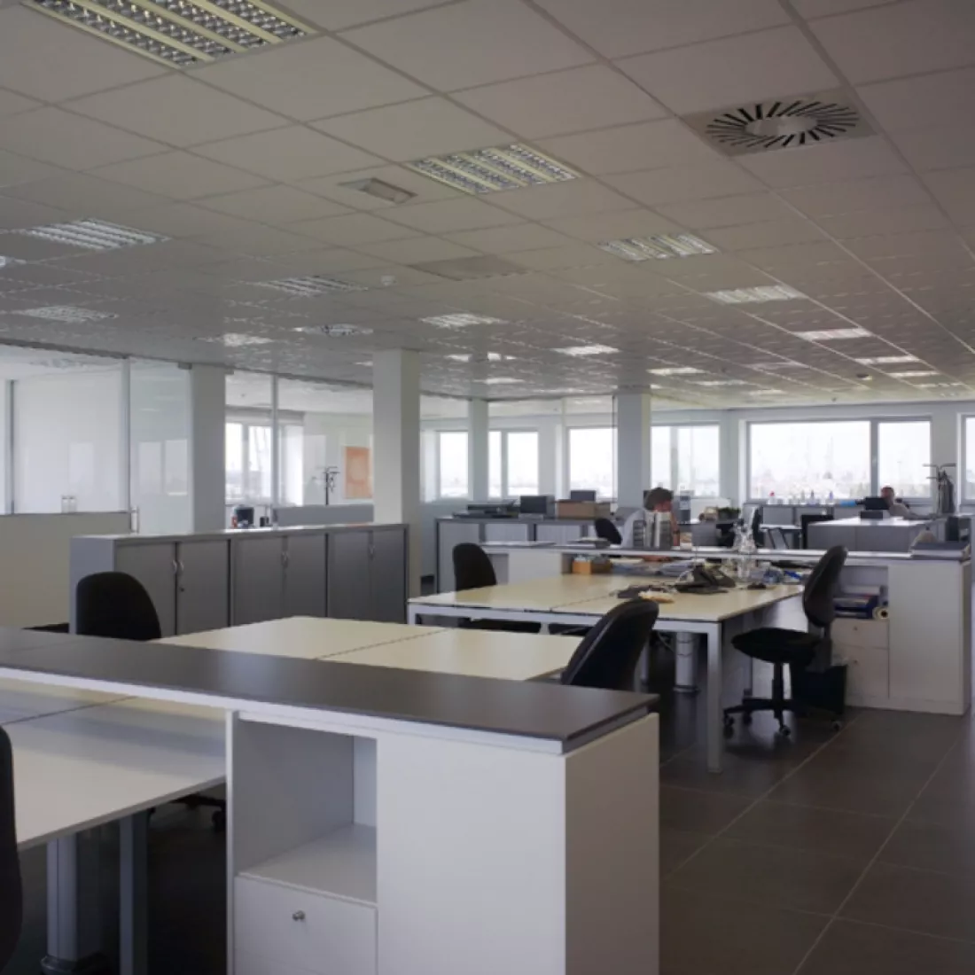 Binnenkant kantoorgebouw Nova Natie HQ. De muren zijn wit en de vloer bevat zwarte stenen. Er staan witte bureaus verspreid over de ruimte.