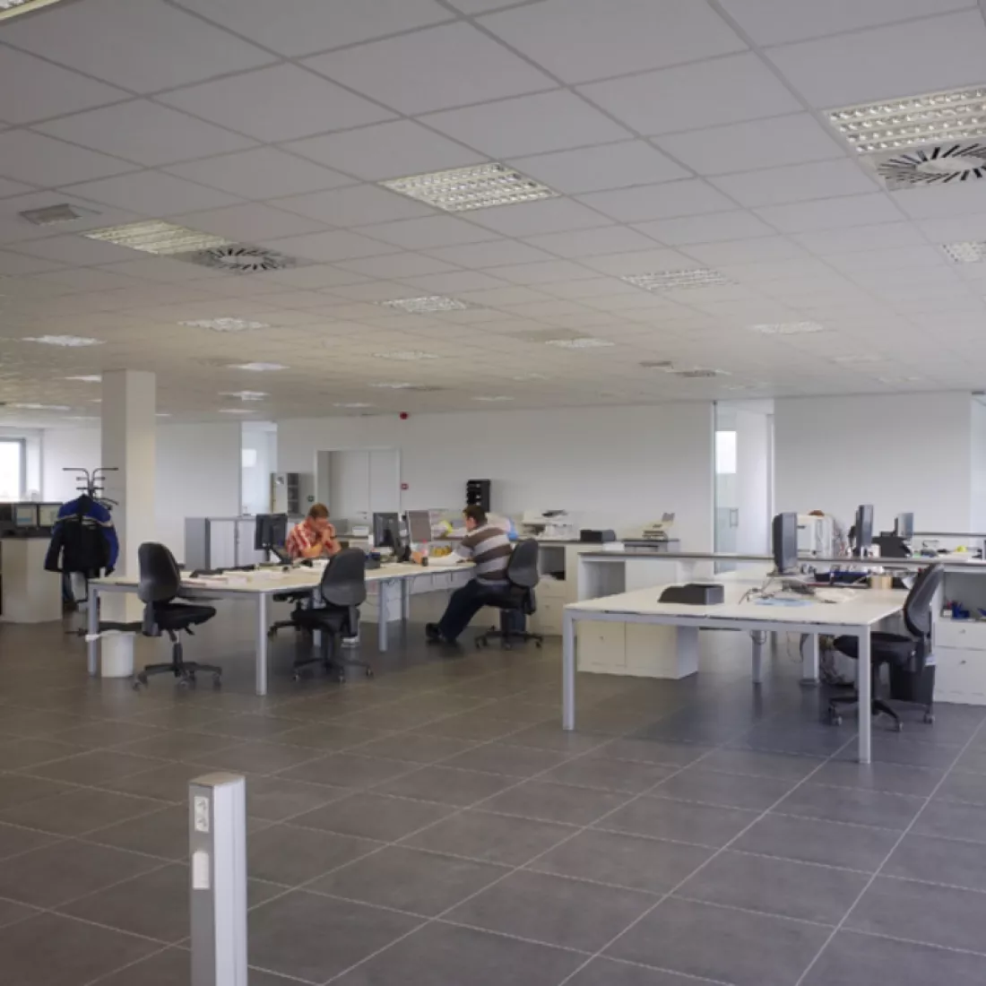 Binnenkant kantoorgebouw Nova Natie HQ. De muren zijn wit en de vloer bevat zwarte stenen. Er staan witte bureaus verspreid over de ruimte.