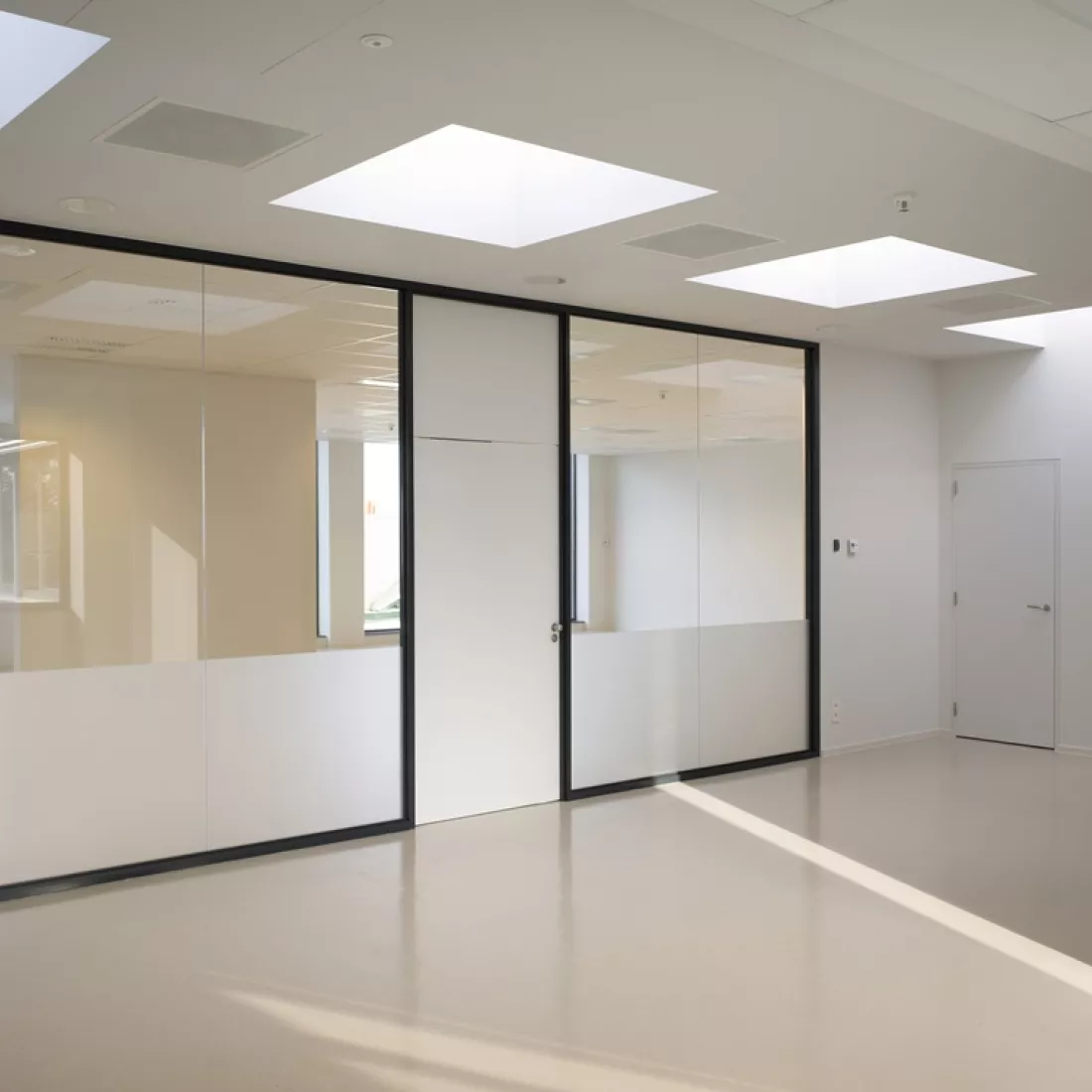 Binnenkant kantoor Cepa. De muren, vloer en het plafond zijn wit. Rechts bevindt zich een witte duur. De achterste muur bestaat uit glas met onderaan een raamfolie. De deur in deze muur bestaat helemaal uit deze folie.