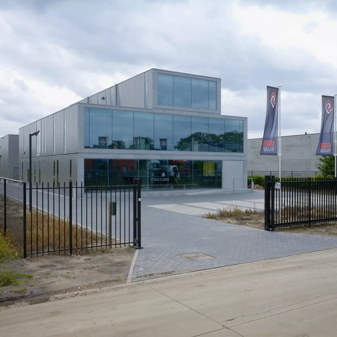 Vooraanzicht kantoor Global Gas Solutions. Rond het kantoor is een zwarte poort. Voor het kantoor zijn parkeerplaatsen voorzien. De voorkant van het kantoor bestaat grotendeels uit ramen.