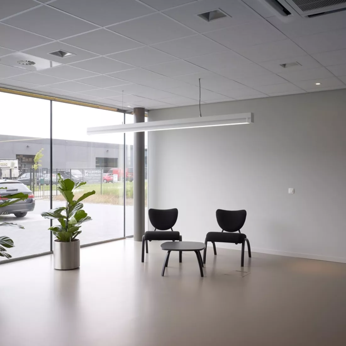 Binnenkant kantoor Global Gas Solutions. Links bevindt er zich een groot raam. Rechts hiervan een witte muur. Voor de muur staan twee zwarte stoelen en een bijzettafel.