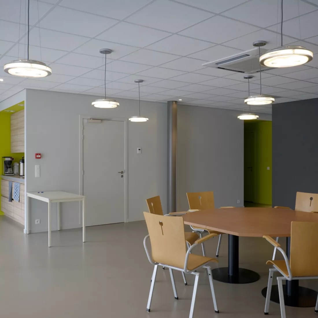 Binnenkant kantoor Global Gas Solutions. Rechts bevindt zich een tafel met stoelen rond. De muur rechts naast de tafel is donkergrijs. Links naast deze muur is er een gang met een groene muur. Helemaal links op de afbeelding bevindt zich een keuken.