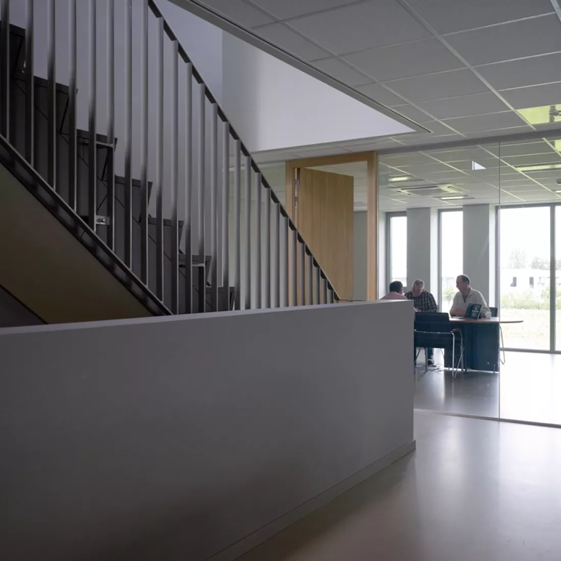 Binnenkant kantoor Global Gas Solutions. Links bevindt zich een zwarte trap met zwarte railing. Tegenover de trap bevindt zich een kantoor. De muur van dit kantoor bestaat uit een glazenwand.