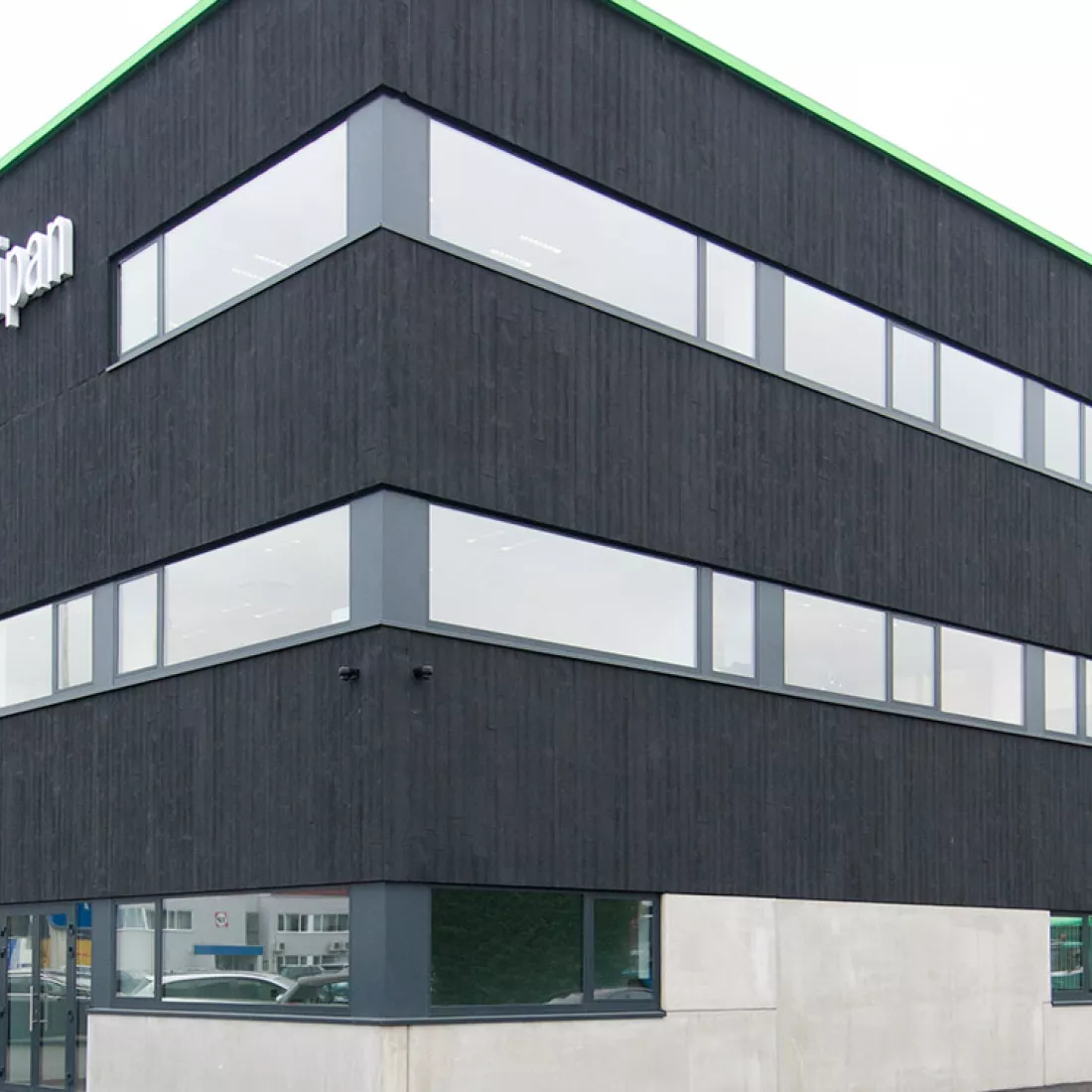 Zijaanzicht kantoor Altripan. Het kantoor is opgebouwd met beton en heeft een zwarte houtlook. Het gebouw bestaat uit drie verdiepingen en heeft op elke verdieping ramen.