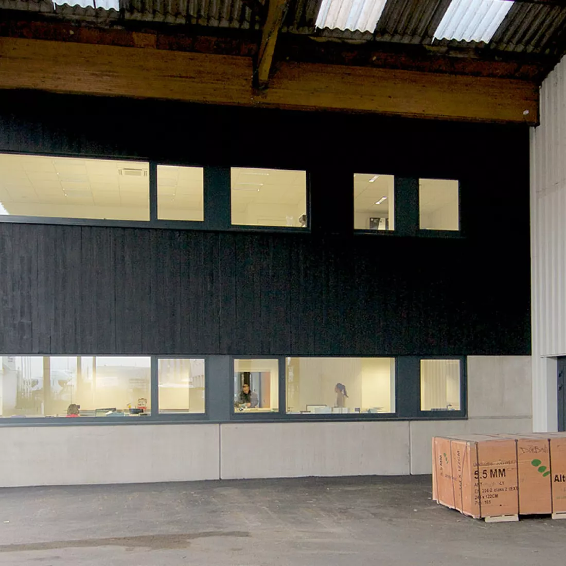 Altripan - zijaanzicht kantoorgebouw. Het gebouw heeft twee verdiepingen en bevat op elke verdieping enkele ramen. Het heeft bovenaan een zwarte houtlook. Er hangt een afdak tegen het gebouw.