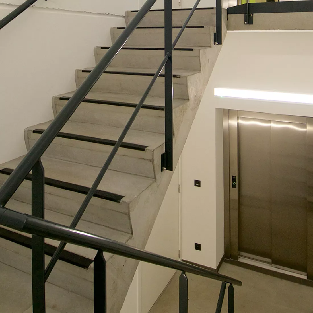 Trappenhal kantoor Altripan. De trap is gemaakt van beton en heeft een zwarte railing. Onderaan bevindt zich een lift.