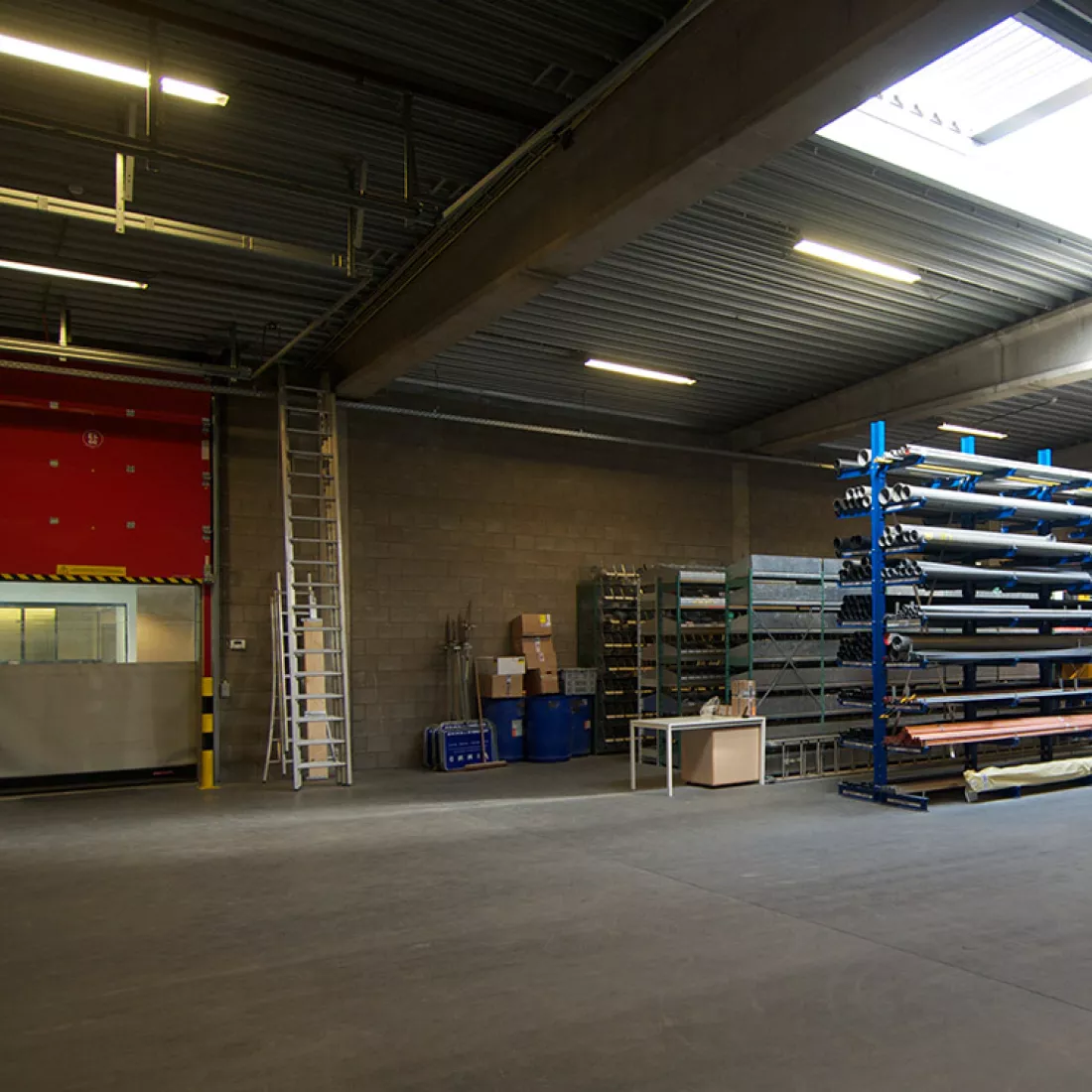 Binnenkant magazijn Vimmo. Links is er een rode poort. Rechts staan rekken met materialen.