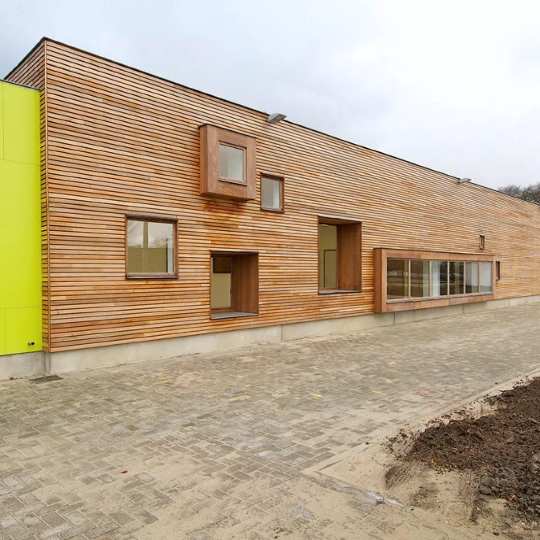 Toonzaal Martens Hout. Het gebouw is opgebouwd uit beton en heeft aan de buitenkant hout. Links bevat het gebouw platen in de kleur van het logo. Het gebouw heeft kleine ramen.