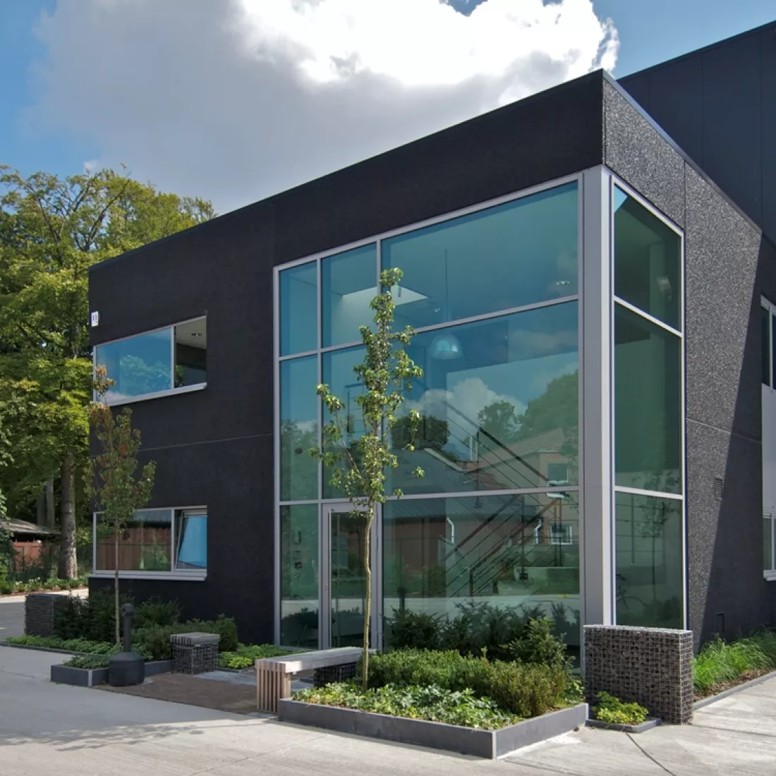 Vooraanzicht kantoorgebouw GRSE. Het gebouw is zwart en bevat enkele ramen. De inkomhal bevat veel ramen. De ramen hebben een grijze omkadering. Het kantoorgebouw bestaat uit twee verdiepingen.