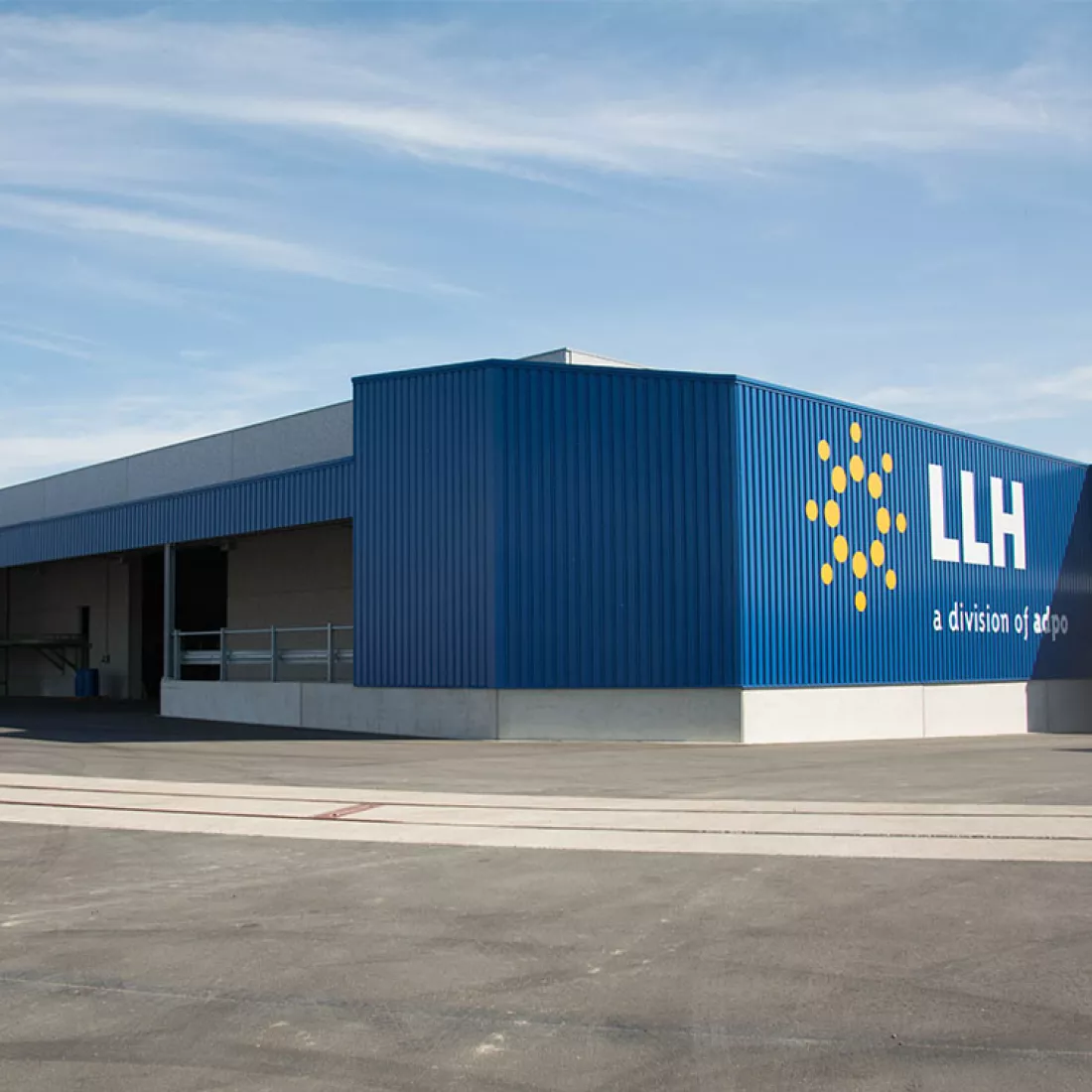 Zijaanzicht Adpo - Adr loods. Het gebouw bestaat uit beton en staal. Het bestaat uit blauwe platen. Rechts hangt het logo van Adpo.