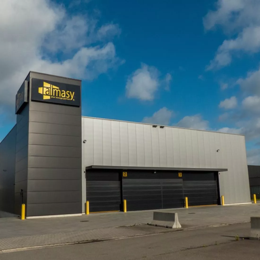 Vooraanzicht industriehal Almasy. De hal is grijs met zwart. De poorten zijn zwart. Het gebouw is gemaakt uit staal.