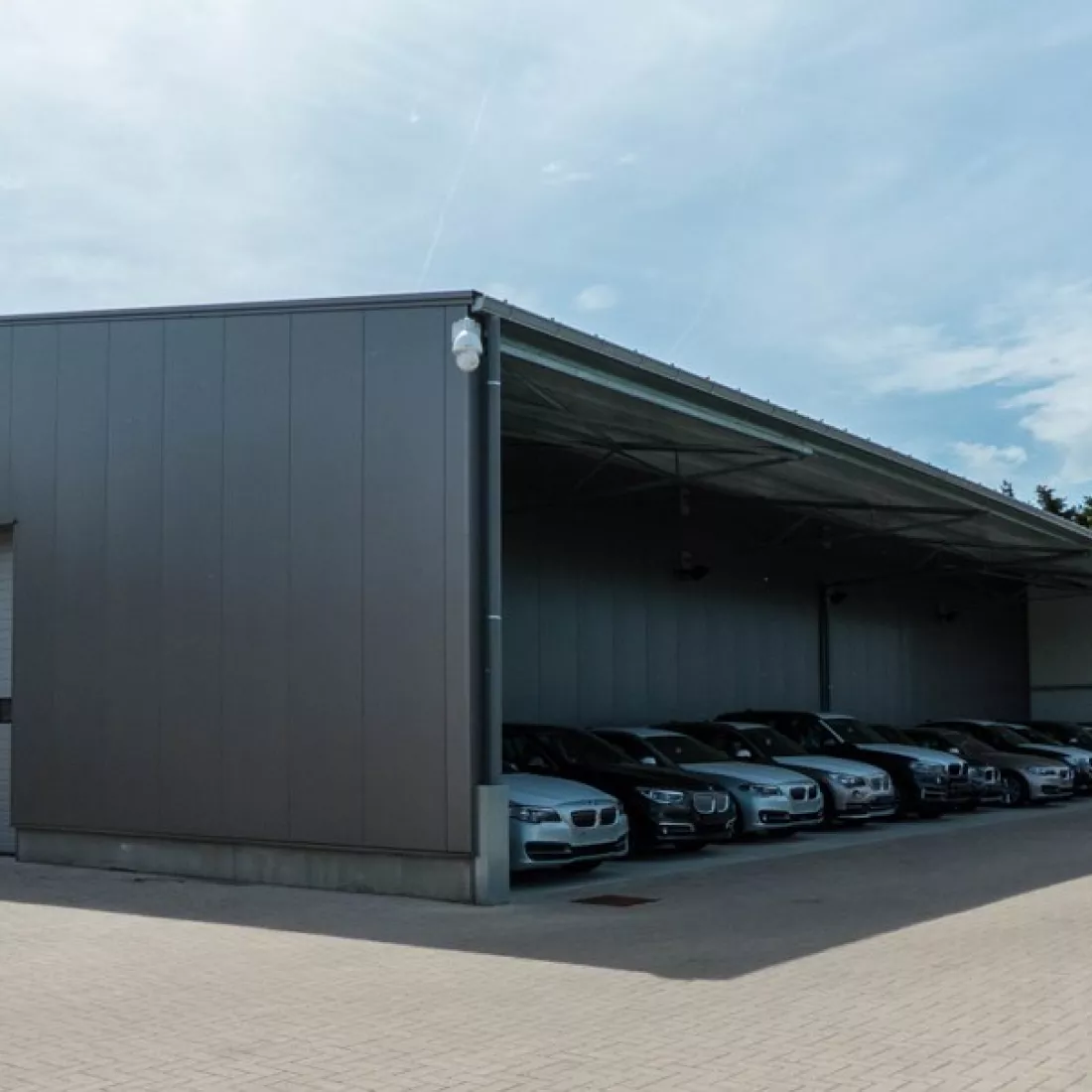 Luifel bandenloods garage Meeusen. De luifel bevat ook muren aan de zijkant. Onder de luifel staan auto's geparkeerd.