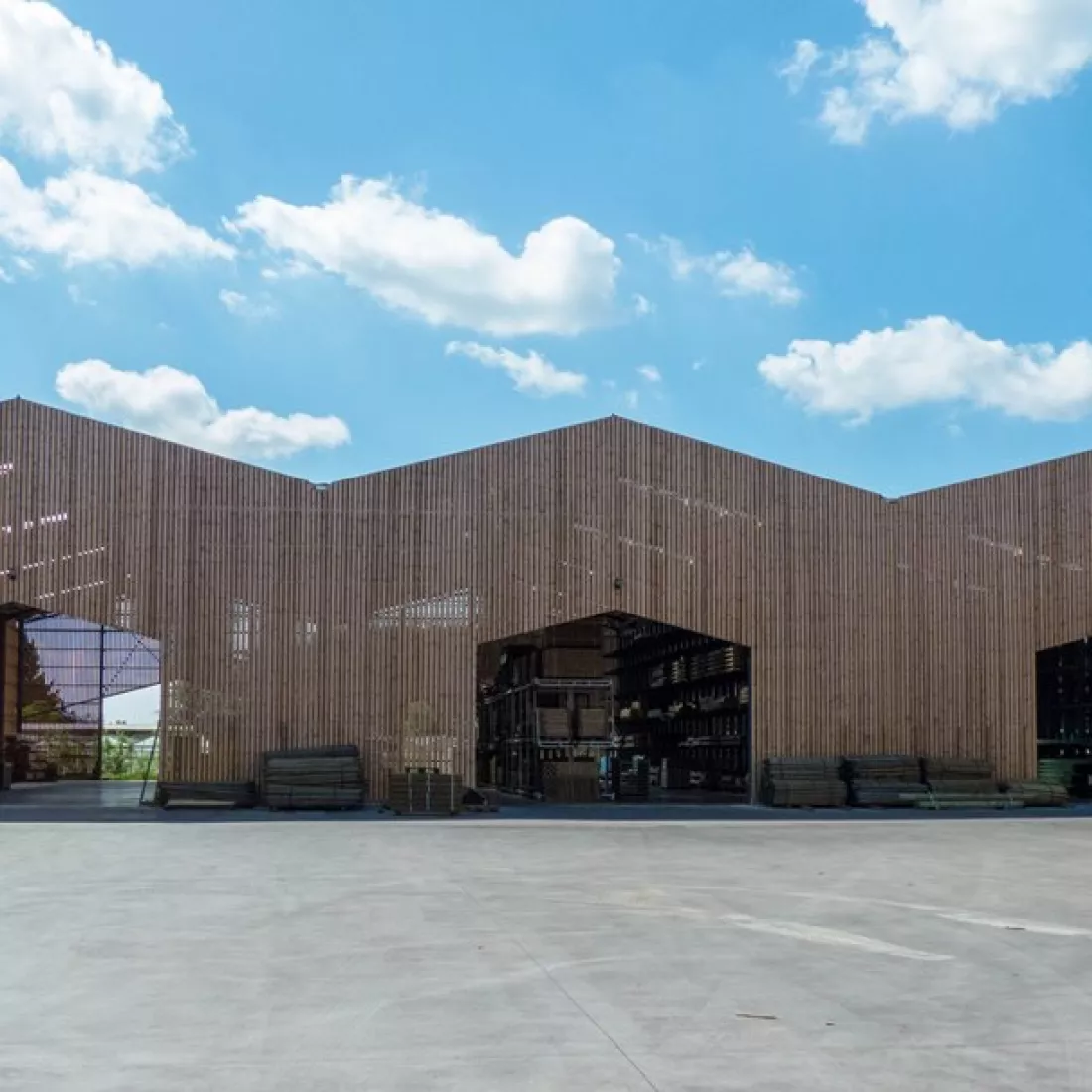 Vooraanzicht opslagplaats Houthandel Janssens. De opslagplaats bestaat ook uit een combinatie van materialen zoals hout. De opslagplaats heeft veel openingen in de vorm van een vijfhoek.