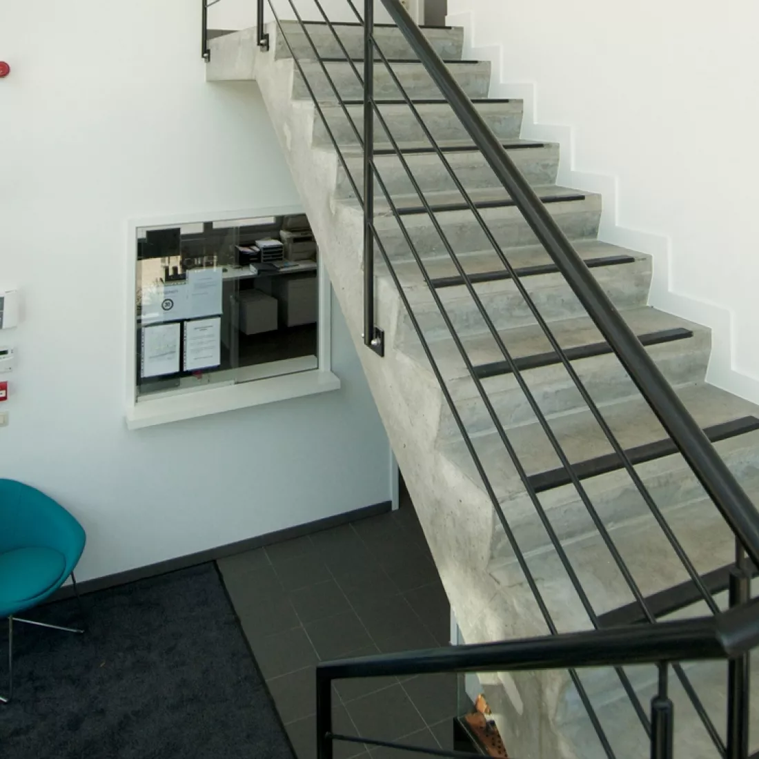 Trappenhal kantoorgebouw GRSE. De trap is grijs en bevat een grijze stalen railing. De muren zijn wit en de vloer zwart.