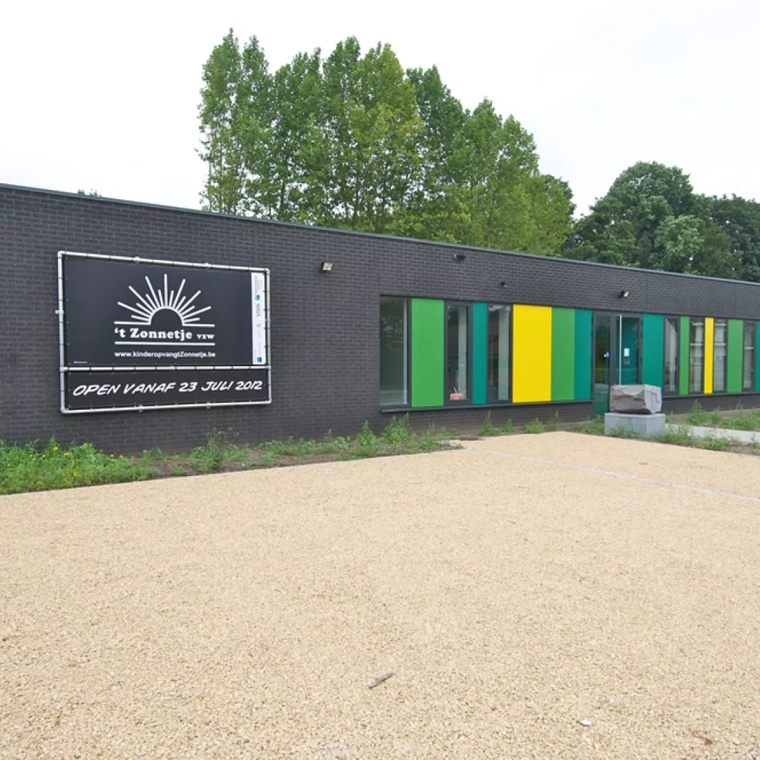 Buitenkant kinderdagverblijf. Het is gemaakt met zwarte steen. Bij de ramen zijn er groene en gele details.