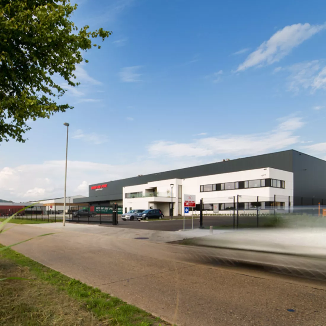 Zijaanzicht magazijn en aanpalend kantoor Van De Pol. Rond het werkterrein bevindt zich een zwart hek met zwarte poort. Het kantoor bestaat uit witte platen en het magazijn uit zwarte platen.