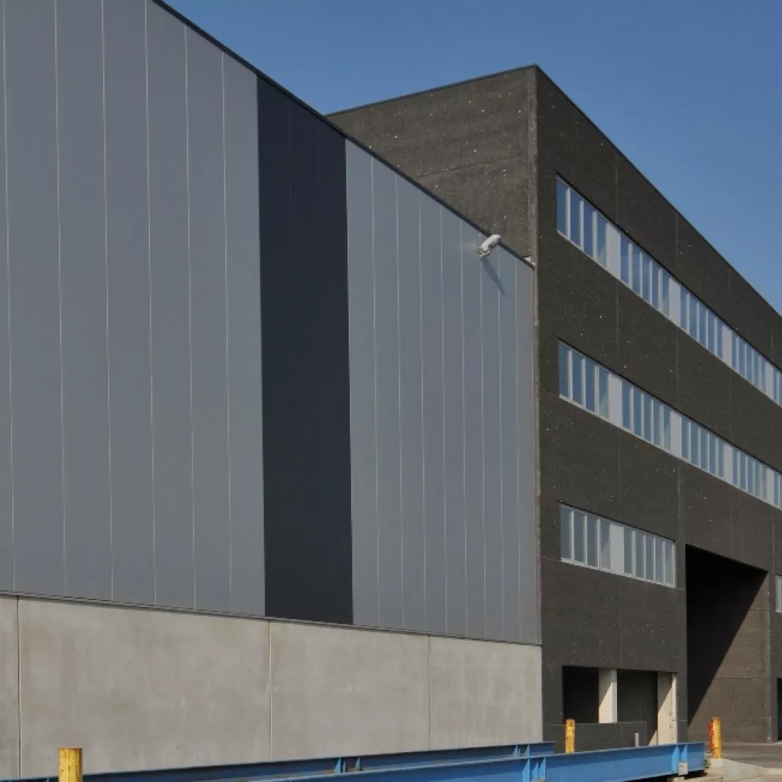 Zijaanzicht kantoor en opslaghal Scheldenatie. Rechts bevindt zich het kantoor en links een deel van de opslagplaats. Het gebouw bestaat uit verschillende tinten grijs.