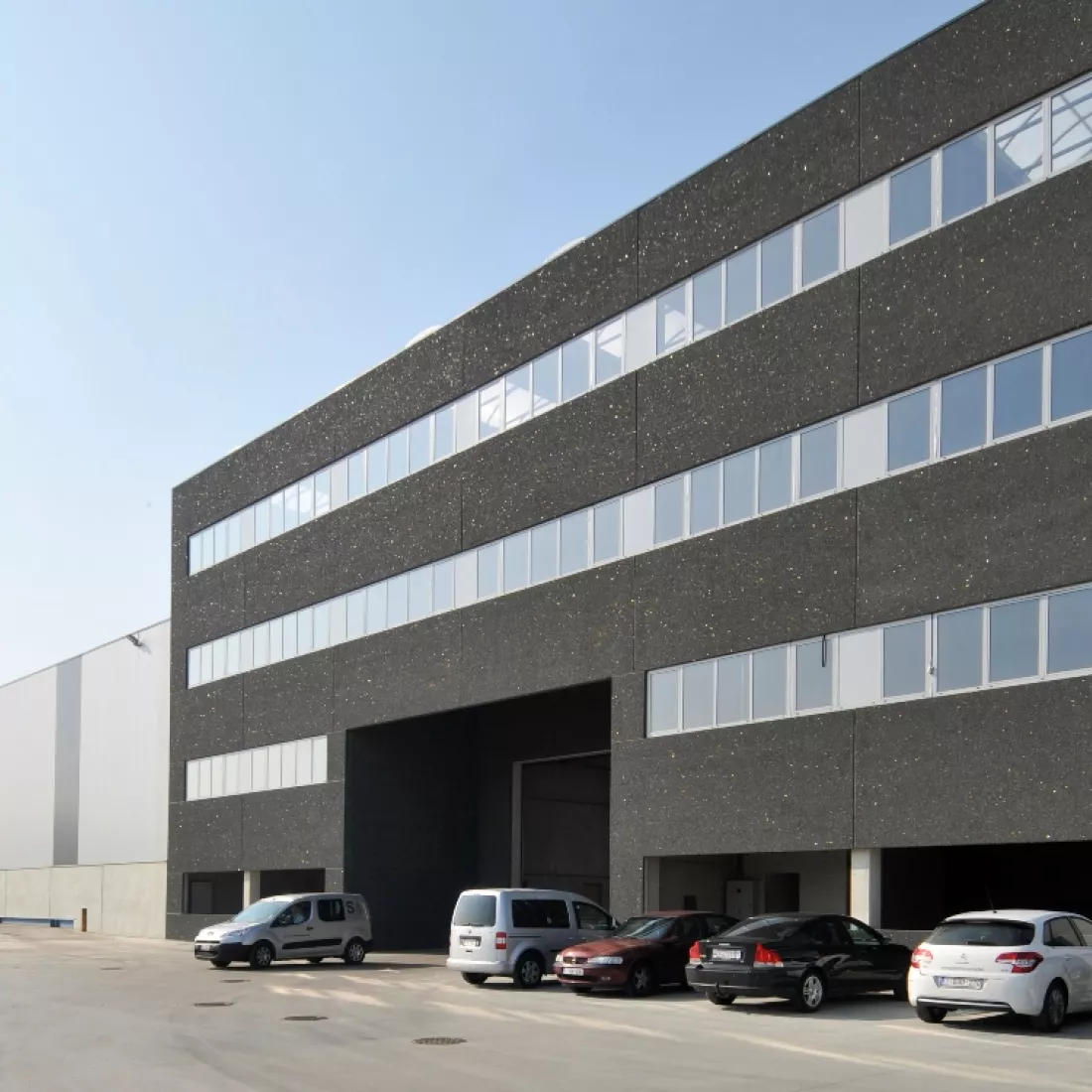 Zijaanzicht kantoor en opslaghal Scheldenatie. Rechts bevindt zich het kantoor en links een deel van de opslagplaats. Voor het kantoor staan auto's geparkeerd.