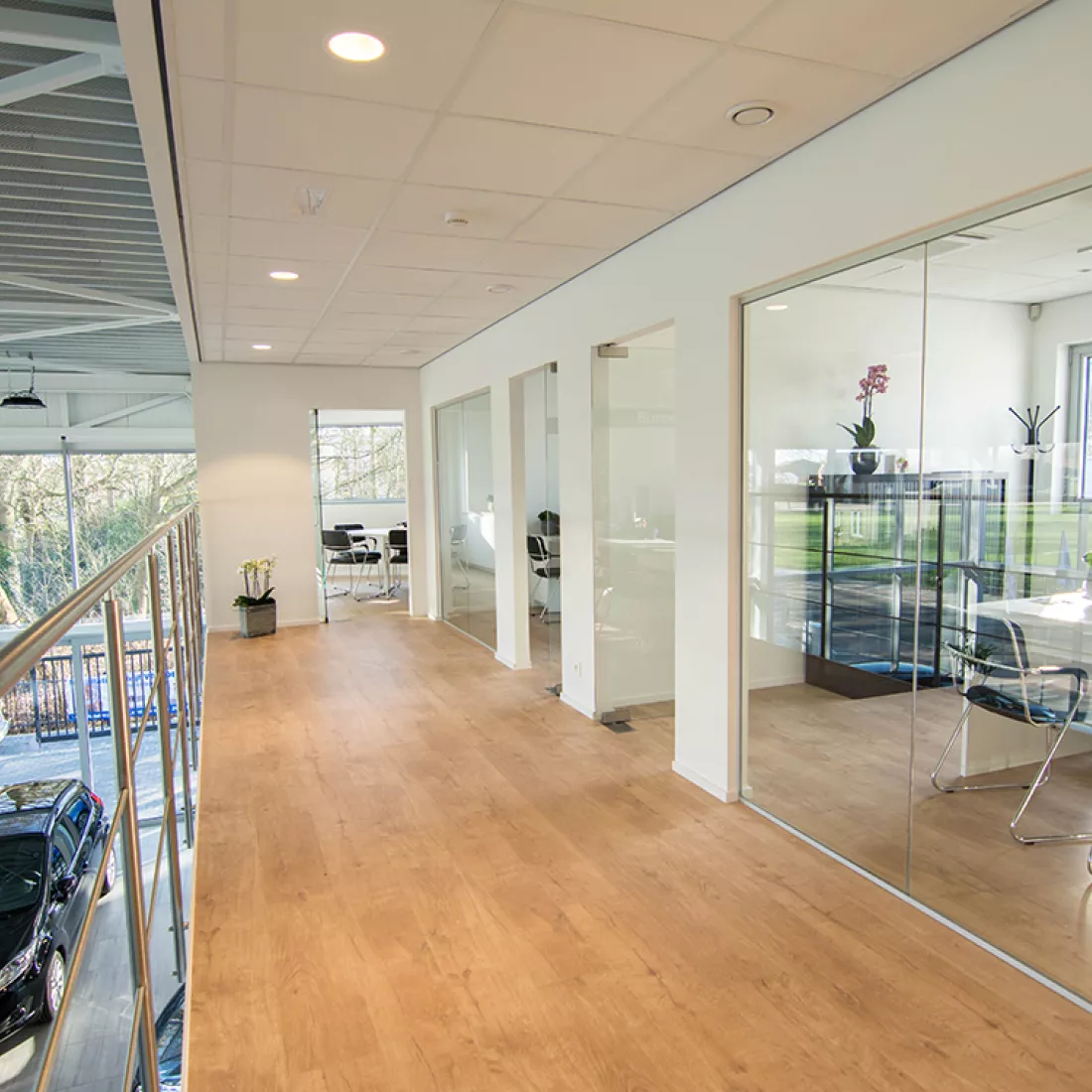 Binnenkant kantoor garage Geudens. Het is op de eerste verdieping. Links is een railing en zie je dat er op de gelijkvloers auto's staan. Rechts zijn kantoren.