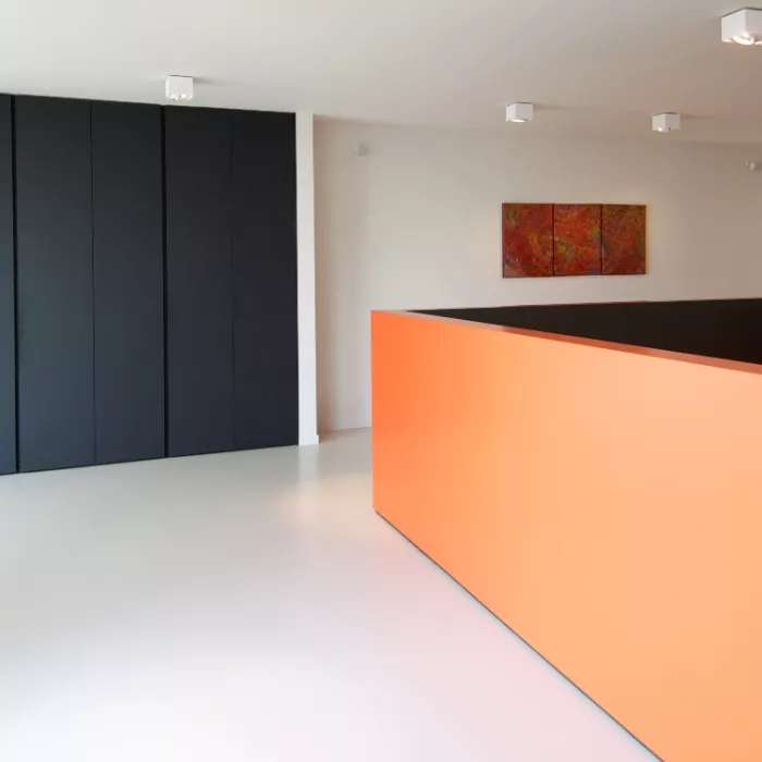 Binnenkant uitvaartcentrum Wase begrafenissen. De muren en vloer zijn volledig wit. De achterste muur heeft links een zwarte inbouwkast en rechts een rood schilderij. Rechts in de ruimte is een oranje lage muur.