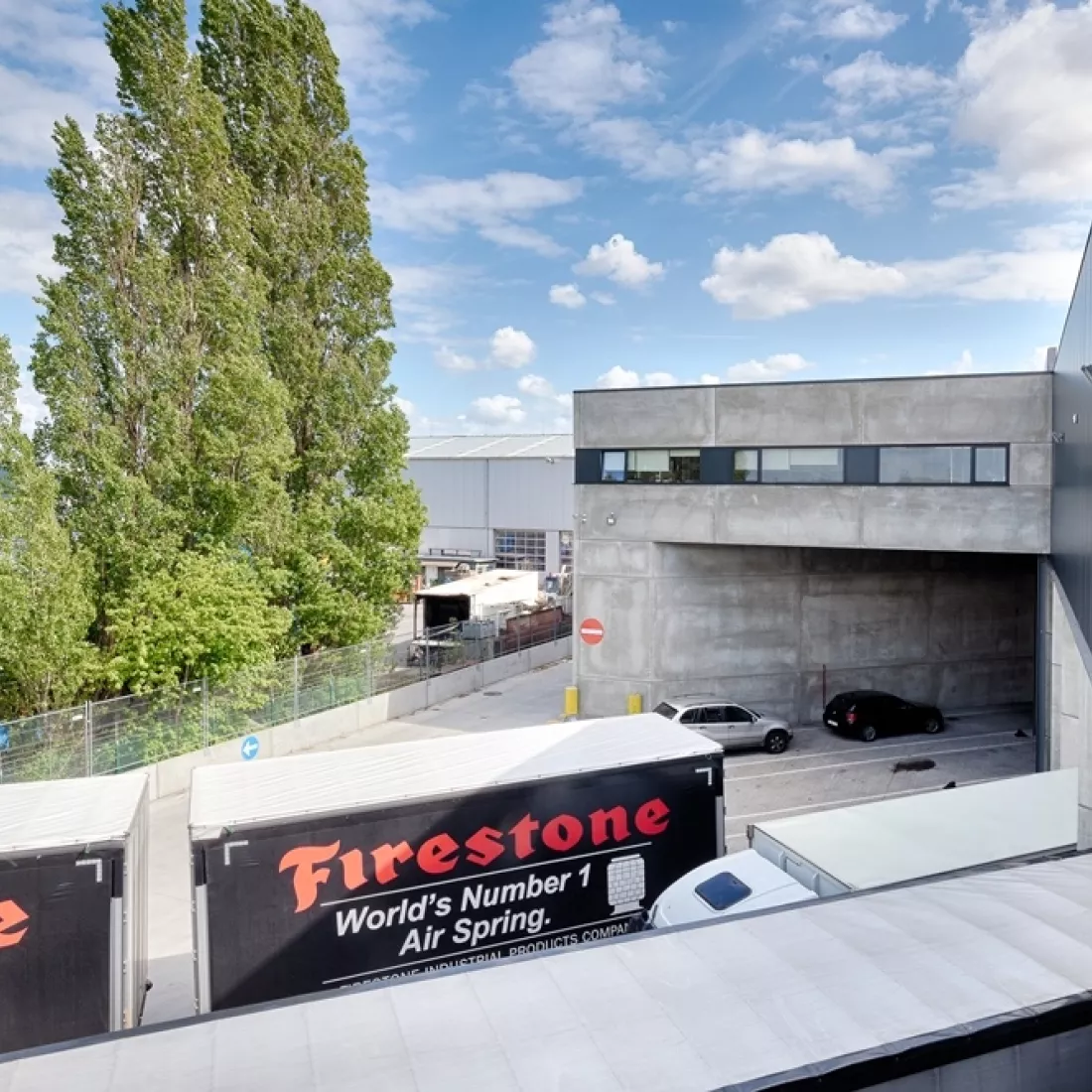 Bovenaanzicht kantoor Transuniverse. Voor het kantoor staan enkele vrachtwagens. Het kantoor is gemaakt uit beton.