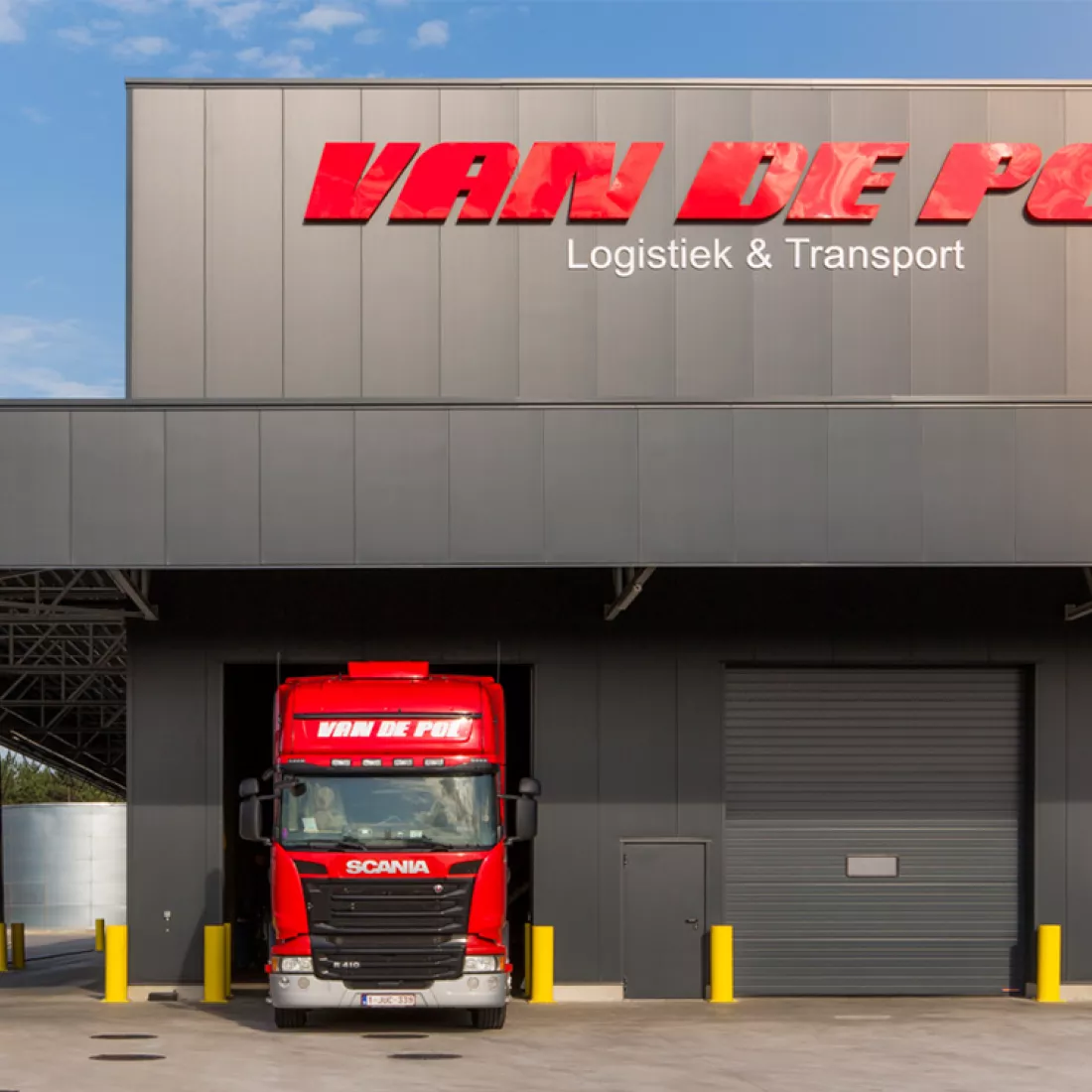 Vooraanzicht magazijn Van De Pol. Het magazijn bestaat uit zwarte platen. De poorten zijn ook zwart. Links bovenaan hangt het logo.