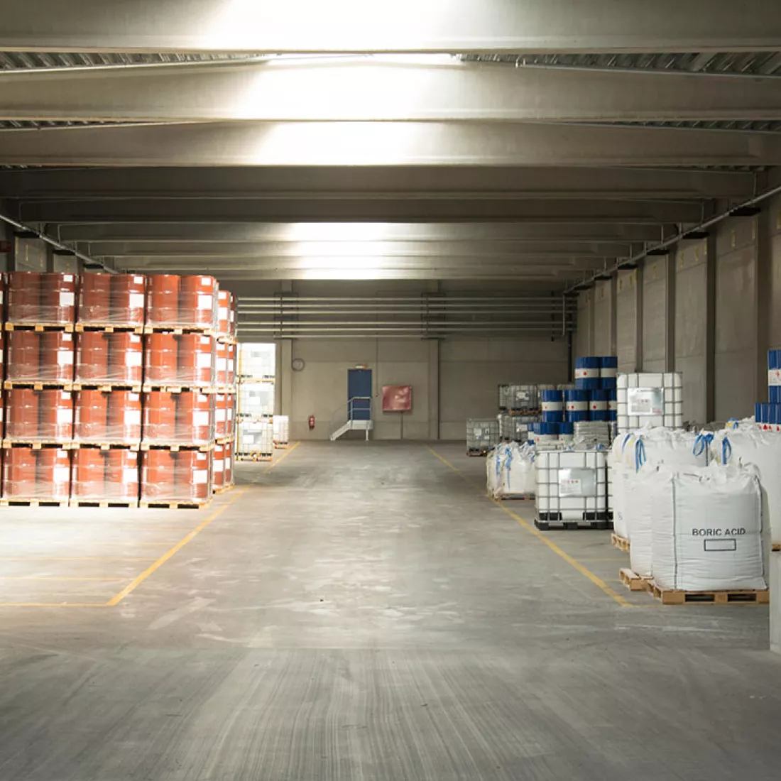 Binnenkant Adpo - Adr loods. In de loods liggen verschillende materialen opgeslagen. De materialen liggen in vakken afgebakend met gele lijnen. Achteraan bevindt zich een blauwe deur.
