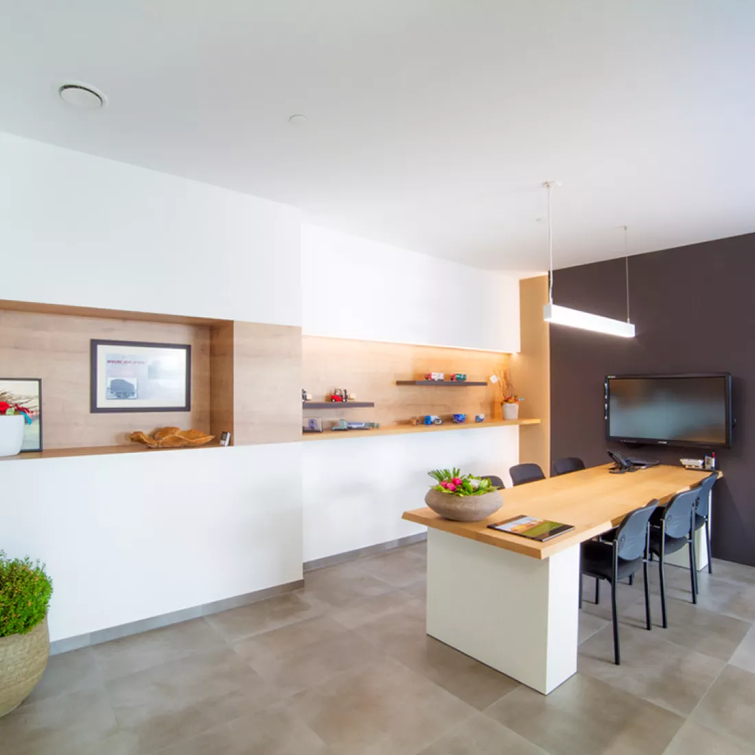 Binnenkant kantoor Van De Pol - vergaderruimte. De muur achteraan is wit en heeft een hout detail?? De muur rechts is zwart en er hangt een TV. Onder de TV bevindt zich een rechthoekige tafel met zes stoelen rond.