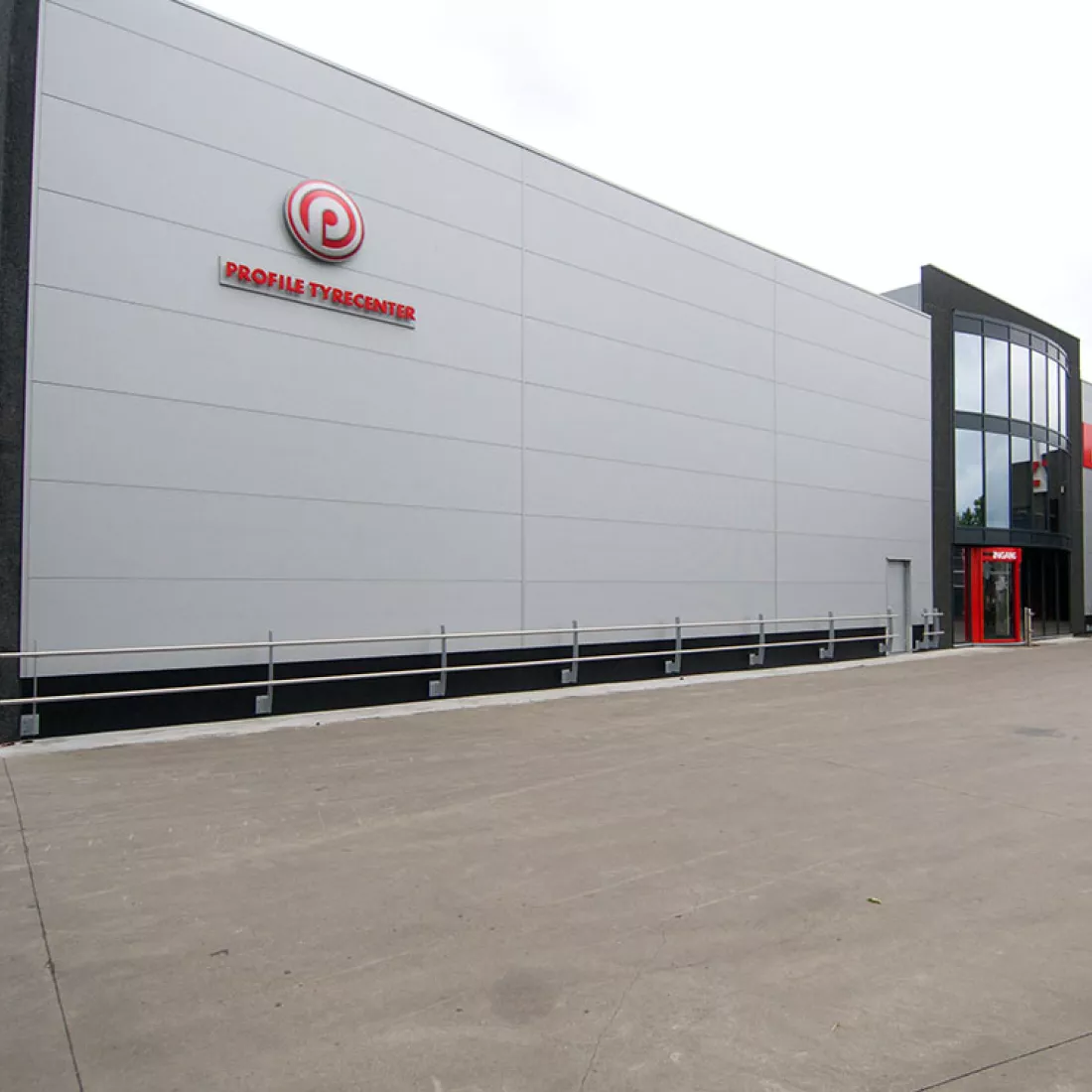 Vooraanzicht TSC. Het gebouw is opgebouwd met een combinatie van materialen. Links bestaat het gebouw uit grijze platen. Links bovenaan hangen rode letters die de woorden "Profile typecenter" vormen. Rechts bevindt zich de inkom. Dit deel van het gebouw is zwart en bevat veel ramen van spiegelglas.