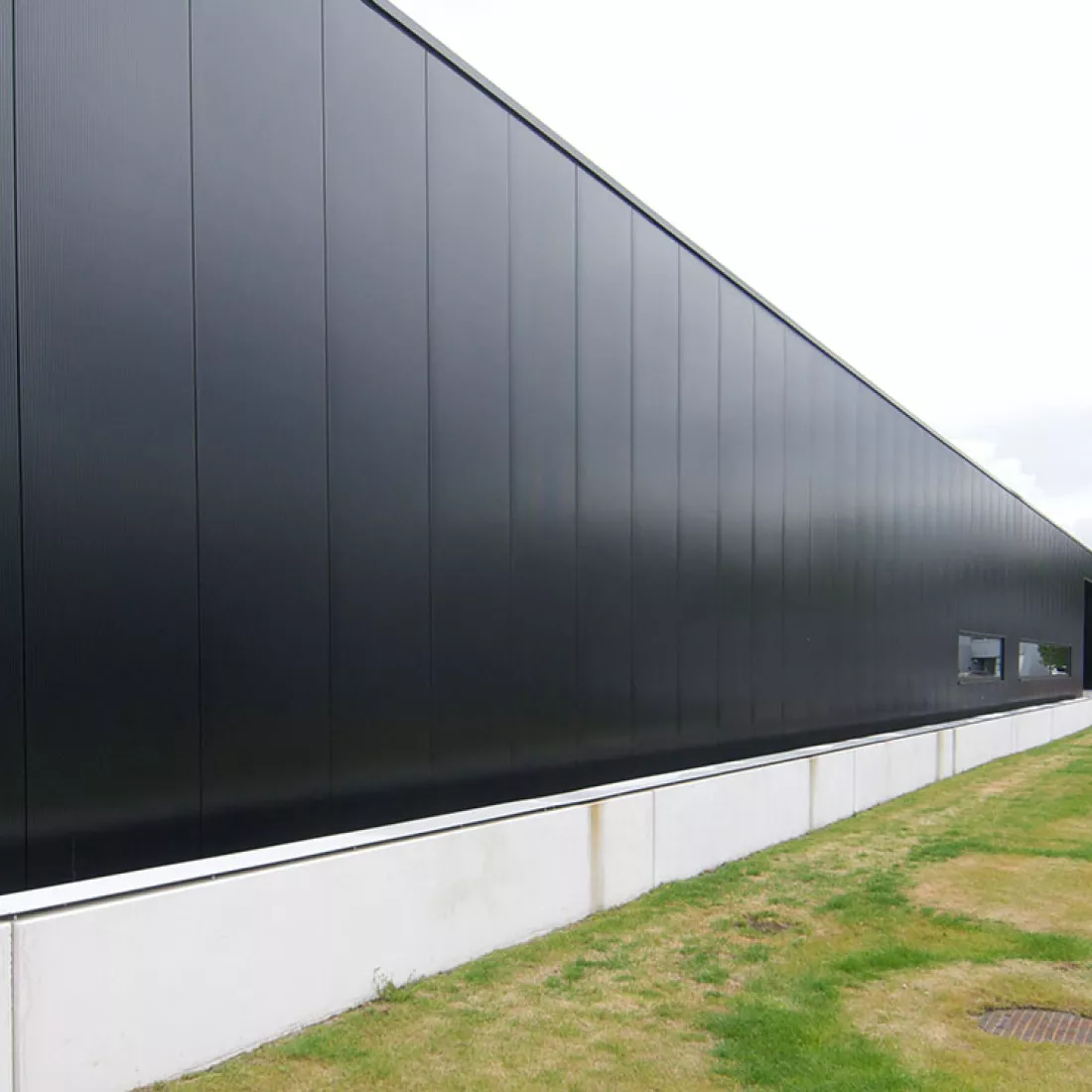 Zijaanzicht productiehal - Reynesco. Dit deel van het gebouw bestaat uit zwarte platen en smalle ramen. Er is een combinatie van materialen gebruikt tijdens de opbouw.