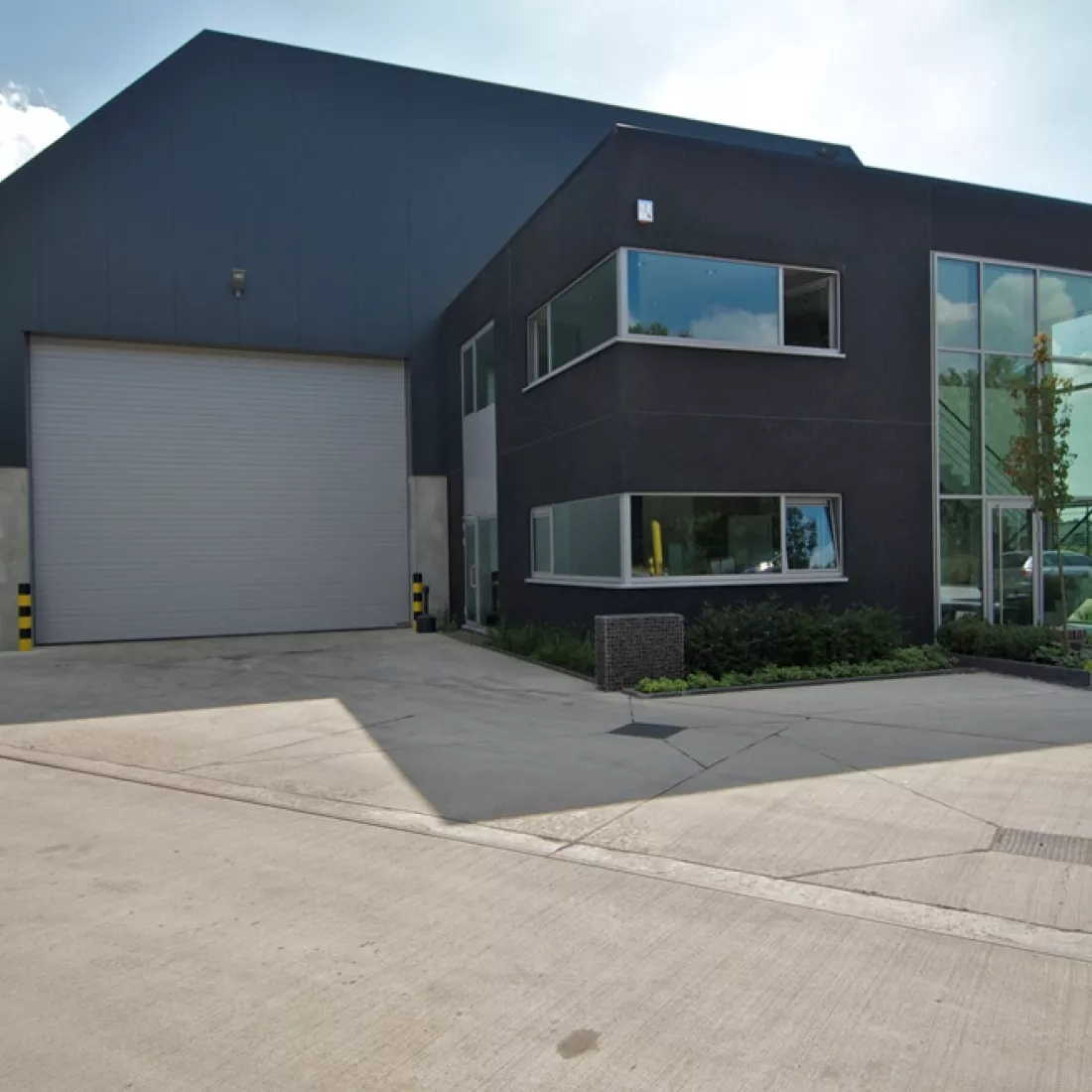 Vooraanzicht kantoorgebouw en opslagplaats GRSE. Het kantoorgebouw bevindt zich voor de opslagplaats. De opslagplaats heeft een grote grijze poort.