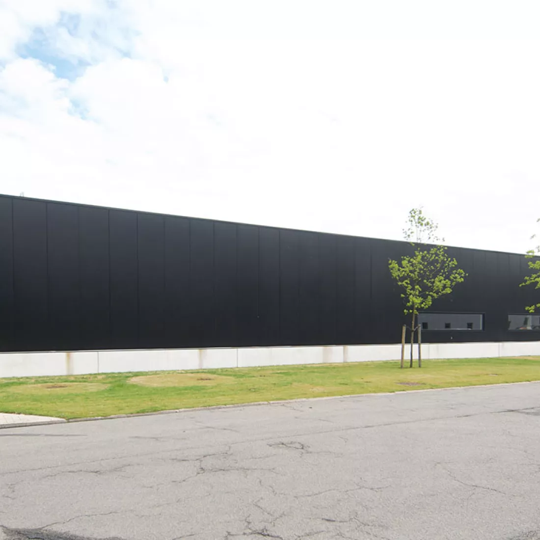 Productiehal - Reynesco. Het gebouw bestaat uit zwarte platen en twee kleine, smalle ramen. Rond het gebouw bevindt zich gras.