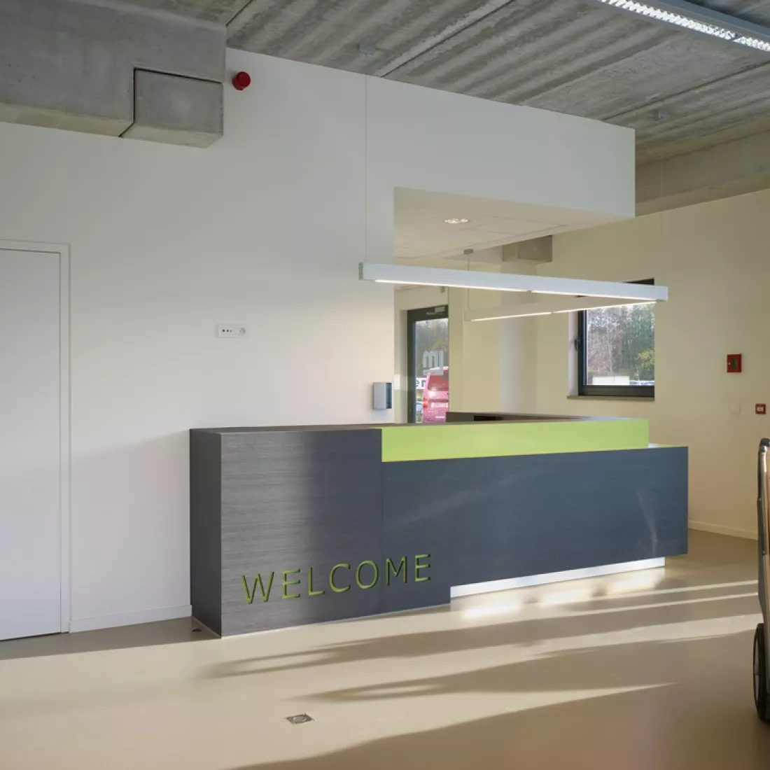 Binnenkant kantoor - DIBO. Dit is een afbeelding van de inkom. Er staat een bruine met groene balie. Rechts onderaan staat het woord "welcome".