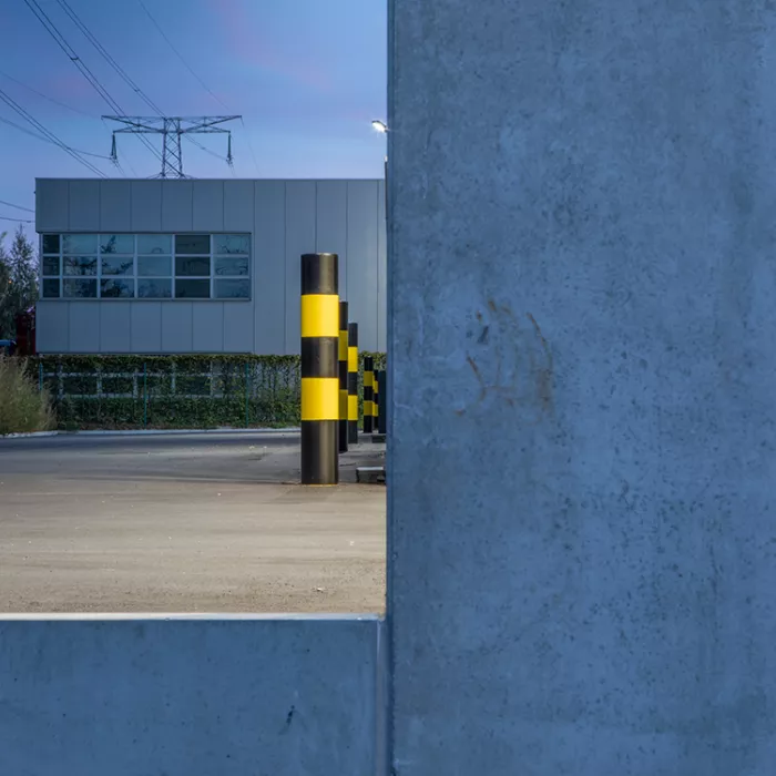 Close-up buitenkant magazijn Corpack. Naast het gebouw staan zwarte palen met gele strepen.