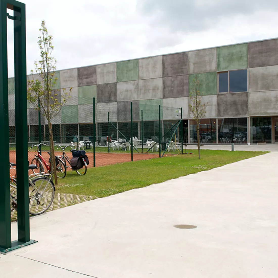 DCA Sportcomplex - buitenkant. De onderste verdieping bestaat uit grote ramen. Links voor het gebouw bevindt zich een tennisveld. 